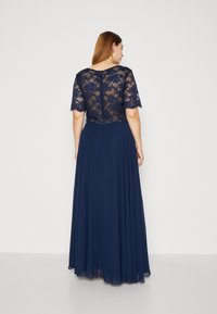 Rochie bleumarin cu un corp dantelat și mâneci scurte. O talie din mărgele evidențiază fusta fluidă, plisată. Detalii subtile de textură și design.
