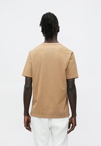 Camisola castanha de algodão com mangas curtas, decote redondo e corte descontraído. Apresenta uma textura lisa e detalhes mínimos de costura.