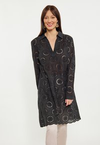 Rochie tunică neagră cu guler, având motive circulare decupate și tiv ondulat. Fabricată din material ușor. Mâneci lungi.