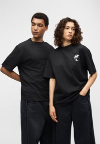 Μαύρα βαμβακερά μπλουζάκια με κοντά μανίκια. Το ένα έχει ένα λευκό λουλουδάτο σχέδιο στο στήθος. Και τα δύο συνδυάζονται με σκουρόχρωμα τζιν παντελόνια.