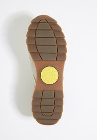 Schoenzool van bruin rubber met een gestructureerd profiel, voorzien van een cirkelvormig geel logo op de hak, bevestigd aan een lichtgrijze bovenkant.