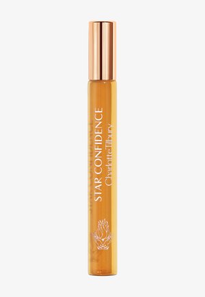 Schlanke bernsteinfarbene Parfümflasche mit roségoldenem Verschluss, beschriftet mit „Star Confidence Charlotte Tilbury“ und einem kleinen Flammen- und Kronensymbol.
