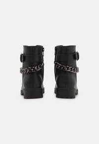 Černé kotníkové boty s hladkým koženým povrchem, které mají boční zip, přezku a kovový řetězový detail na zadní straně.