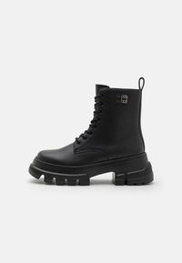 Botines negros con cordones hechos de cuero sintético. Presentan una suela gruesa y texturizada, y una lengüeta en la parte trasera. Sutil branding en el costado.