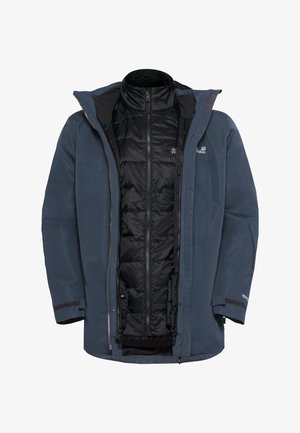 Giacca esterna spessa di color blu scuro con una fodera interna isolante nera rimovibile, frontale con zip e polsini regolabili. Presenta il logo e materiale impermeabile.