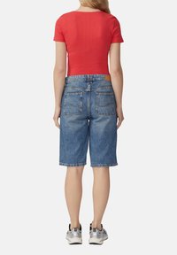 Czerwyn ribbed bluzka z krótkim rękawem w połączeniu ze średnio-pranym dżinsowym szortami Bermuda. Szorty mają tylną kieszeń i luźny krój. Srebrne buty sportowe.