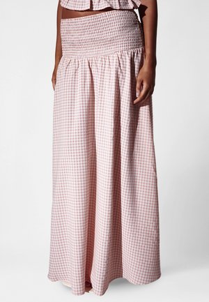 Donna che indossa una gonna lunga a vita alta con motivo a quadretti rosa e bianco, con fascia elastica arricciata e tessuto fluente.