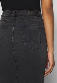 Černá džínsová sukně s mírně zvýšeným pasem, která má dvě zadní kapsy, tónové prošití a koženou nášivku s logem na pasu.