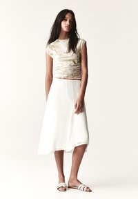 Top à manches courtes à motifs floraux en tissu doux ; jupe midi blanche fluide avec taille élastique ; portée avec des sandales en beige à lanières.