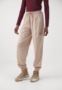 Persoon in beige cargo pants met elastische boorden en een bordeauxrode lange mouwtrui, gecombineerd met beige hoge sneakers.