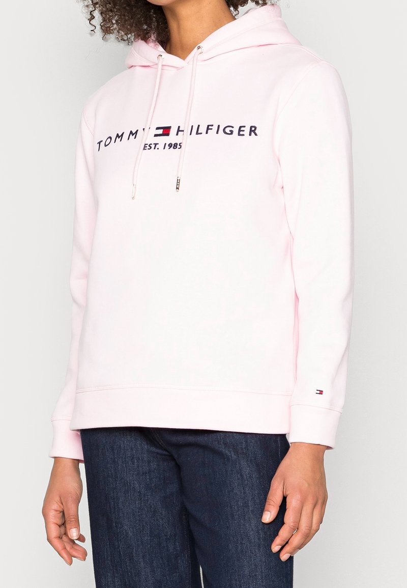 Felpa con cappuccio rosa chiaro con logo "TOMMY HILFIGER" in contrasto navy e anno di fondazione. Presenta coulisse e polsini a coste.