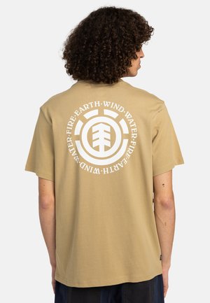 Beige tričko s krátkým rukávem, které na zadní straně zdobí velká bílá kulatá grafika s elementárními symboly. Vyrobeno z měkkého bavlněného materiálu.