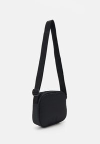Czarna prostokątna torba na ramię z regulowanym paskiem zawieszona na białym tle.