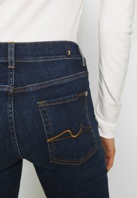 Donkerblauwe denim jeans met een aangesloten ontwerp. Heeft een gouden accentsteek op de achterzak en een klein logotag vlakbij de tailleband.