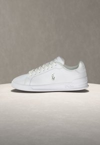 Λευκό χαμηλό sneaker με κορδόνια, μικρό λογότυπο Polo στο πλάι και ελαστική σόλα τοποθετημένο σε φωτεινή επιφάνεια.