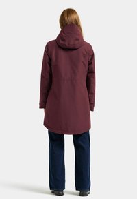Marin vattentät jacka med huva, midilång design, med en subtil logotyp på baksidan och matchad med mörka jeans.