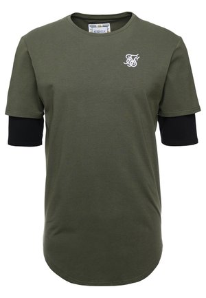 Olivgrünes Kurzarm-T-Shirt, getragen über schwarzen Langarmärmeln, mit weißem, gesticktem Logo auf der linken Brust.