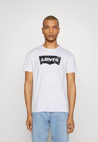 Hvit bomulls t-skjorte med svart Levi's-logo grafikk på brystet. Rund hals, korte ermer og en avslappet passform.