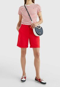 Shorts en coton rouges avec ourlet retourné, associés à un t-shirt rayé blanc et rouge. Accessoirisés avec un sac bandoulière noir et blanc et des chaussures bateau.