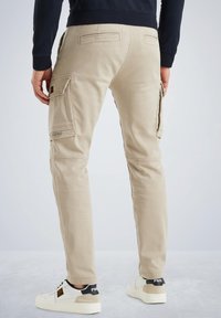 Beige cargo bukser med flere sidelommer og stikninger, med en slim fit og lavet af bomuldsstof. Sammen med hvide sneakers.