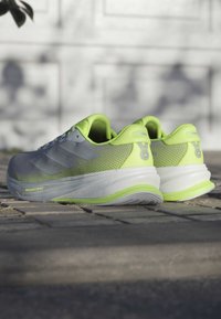Szare buty sportowe z neonowozielonymi akcentami, z teksturowaną siateczkową górą, wyposażone w trzy szare paski, wyściełaną podeszwę oraz gładką konstrukcję pięty.