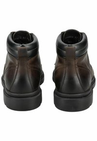 Botas de tobillo de cuero marrón con acentos negros, textura suave, punta redondeada y suela de goma resistente. Presenta un detalle de costura mínimo.