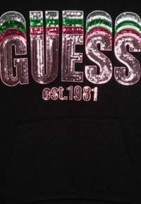Felpa nera con ampie lettere in paillettes multicolori "GUESS" e "est. 1981." Tessuto morbido con tasca frontale.