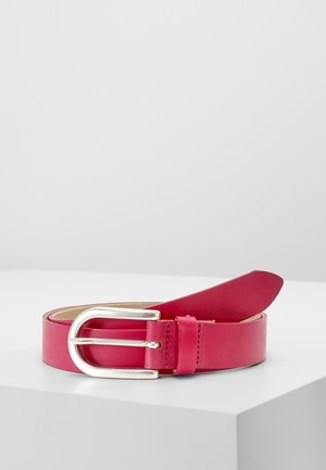 Ceinture en cuir rouge avec boucle en métal argenté, enroulée sur une surface blanche avec un fond gris clair neutre.