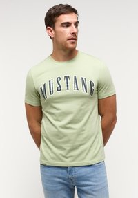 Világoszöld pamut póló kerek nyakkivágással és rövid ujjakkal, az elején sötétkék "MUSTANG" felirattal.