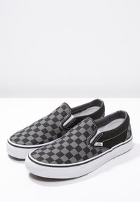 Chaussures à enfiler à damier noir et gris avec une tige en toile, une semelle en caoutchouc blanche et des accents noirs contrastants.