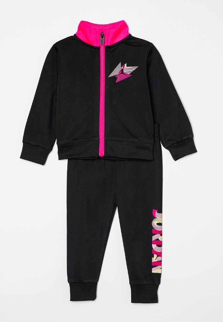 Survêtement noir pour enfants avec fermeture éclair et col rose fluo, arborant un logo Jordan rose sur la poitrine et le texte multicolore "JORDAN" sur la jambe gauche.