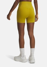Hoge taille, gele sportshorts met een gladde textuur, die tot halverwege de dijen reiken, gecombineerd met witte schoenen en enkel sokken.