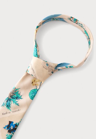 Cravate beige avec un motif floral dans des nuances de bleu, jaune et vert, nouée en un nœud lâche sur fond blanc.