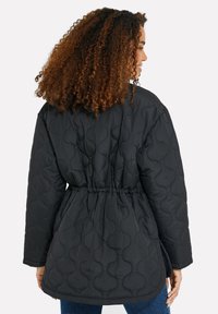 Chaqueta negra acolchada con cintura ajustada, que presenta un patrón texturizado y un corte relajado. Mangas largas y dobladillo redondeado.