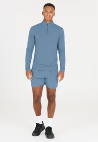 Ljusblå långärmad sporttröja med dragkedja, i kombination med matchande shorts. Svarta träningsskor och vita ankelsockor fulländar outfiten.