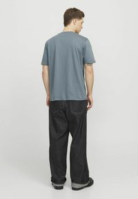 Tricou albastru cu mânecă scurtă, fabricat din bumbac, asociat cu o pereche de blugi închiși la culoare, largi, cu tivuri răsucite și cusături vizibile.