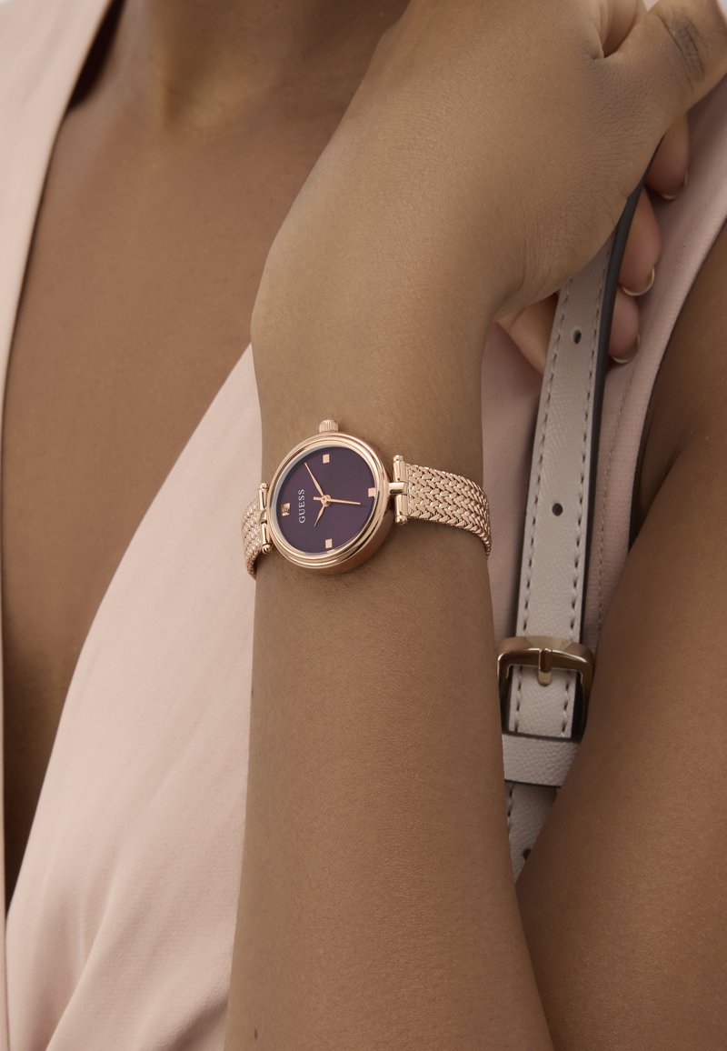 Roosa kuldne kell ümmarguse tumesinise kellakoonusega, millel on kudumiselt metallist rihm. Rihm on detailsete tekstuuride ja siledanappa.