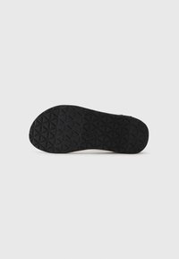 Suela de zapato de goma negra con un patrón de relieve geométrico, diseño plano y el nombre de la marca en relieve. Textura suave con una construcción resistente.