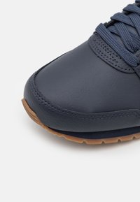 Marinblå lädersneakers med texturerad yta, rund tå och kontrasterande gummisula. Har matchande snörning och stickade detaljer.