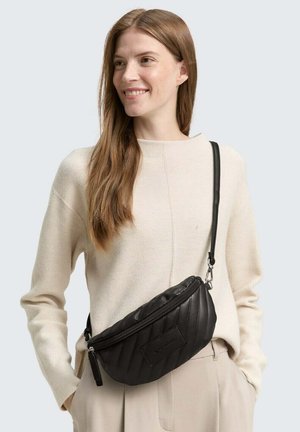 Schwarze, gesteppte Umhängetasche aus Leder mit Reißverschluss und verstellbarem Träger, getragen über einem cremefarbenen Pullover.