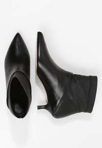 Bottes noires jusqu'à la cheville en cuir lisse avec un embout pointu, un talon fin et un détail en tissu doux au niveau de la cheville.