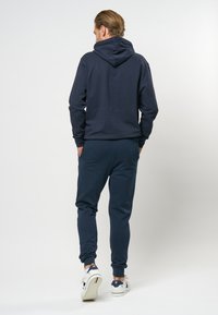 Donkerblauwe hoodie en joggingbroek gemaakt van zachte stof. De hoodie heeft een trekkoord en een kangoeroezak. Witte sneakers maken de casual look af.