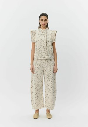 Blomstret todelt sæt i cremefarvet stof. Toppen har flæseærmer og knapper; brede bukser med matchende blomsterprint. Bæres med vævede sko.