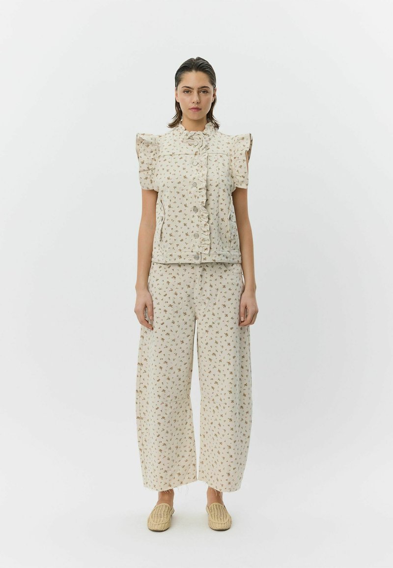 Blomstret todelt sæt i cremefarvet stof. Toppen har flæseærmer og knapper; brede bukser med matchende blomsterprint. Bæres med vævede sko.