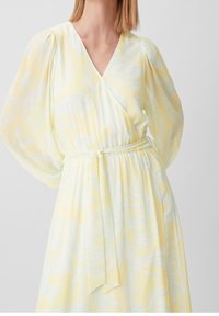 Keltainen kimono-mallinen mekko, jossa on hienovarainen lehtikuvio, puffihihat ja solmittava vyötärötyylitys. Valmistettu kevyestä ja valuvaasta kankaasta.