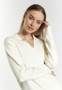 Cream-colored pullover sweater with a notch collar, long sleeves, and a soft texture, featuring minimal seams and a relaxed fit.