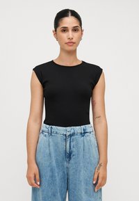 Zwarte fitted top met korte cap mouwen, van zacht geribbeld materiaal. Gecombineerd met lichtblauwe denimbroek met hoge taille en een ceintuur.