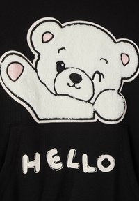 Felpa nera con una grafica di un orso bianco peloso che fa l'occhiolino e alza una zampa. Testo "HELLO" in un font giocoso bianco sotto il design.