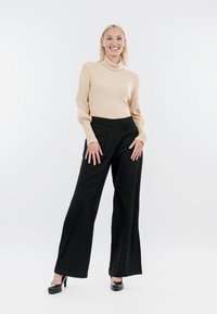 Beige geribbelde coltrui en zwarte wijde broek. De outfit heeft een soepele textuur en wordt aangevuld met zwarte hoge hakken.