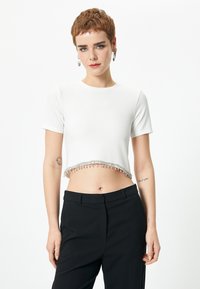 Hvid cropped t-shirt med korte ærmer, med en perlekant. Kombineret med sorte højtaljede bukser. Glat tekstur.